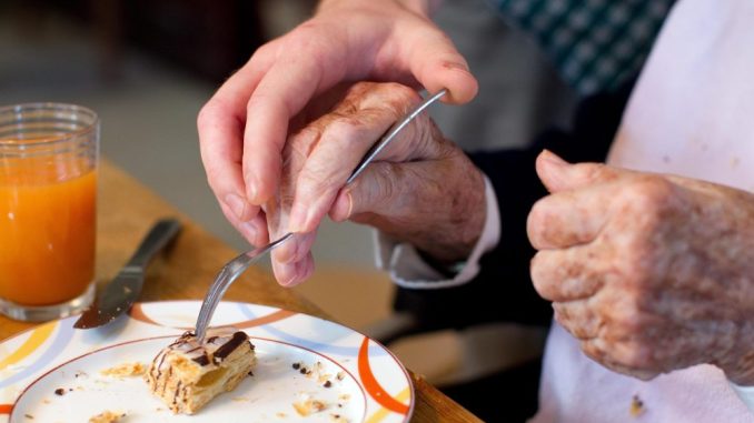 Ein Mann hilft einer alte Frau beim Einnehmen einer Mahlzeit. Foto: Friso Gentsch/Archiv